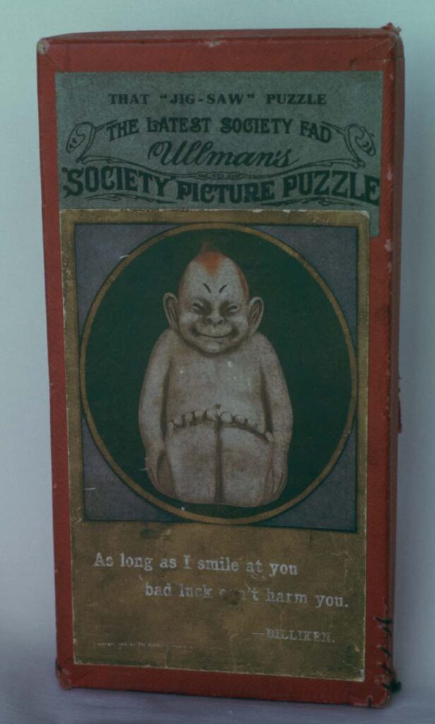 Cover of box for billiken puzzle. Cardboard. 1908